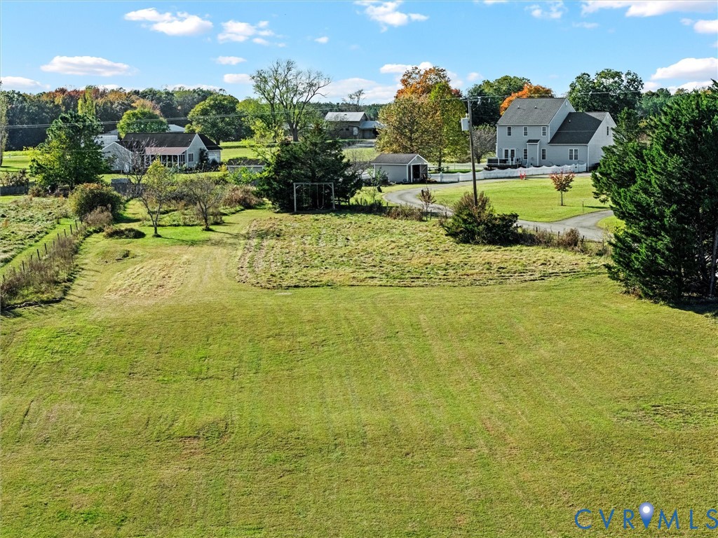 Aerial view of a broad grassy property with neighboring homes, trees, and a curving driveway.