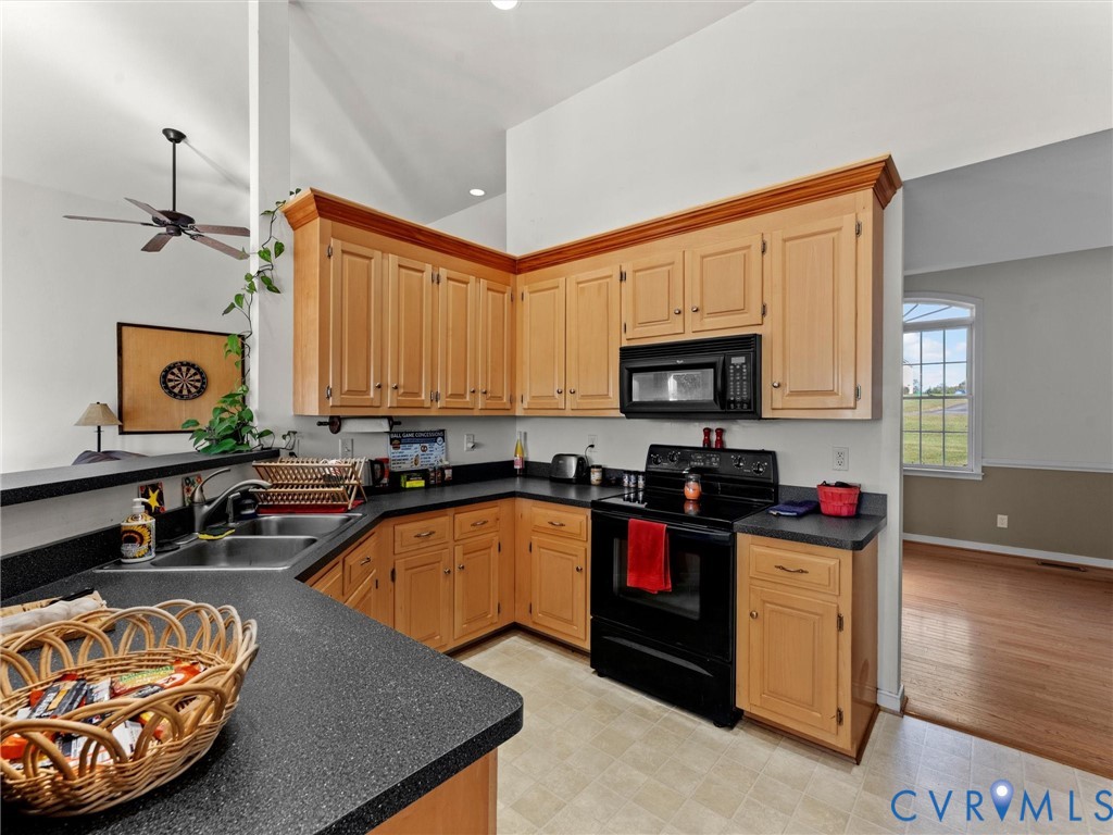 Kitchen with honey-colored cabinets, dark countertops, and black appliances beside a bright adjoining room.