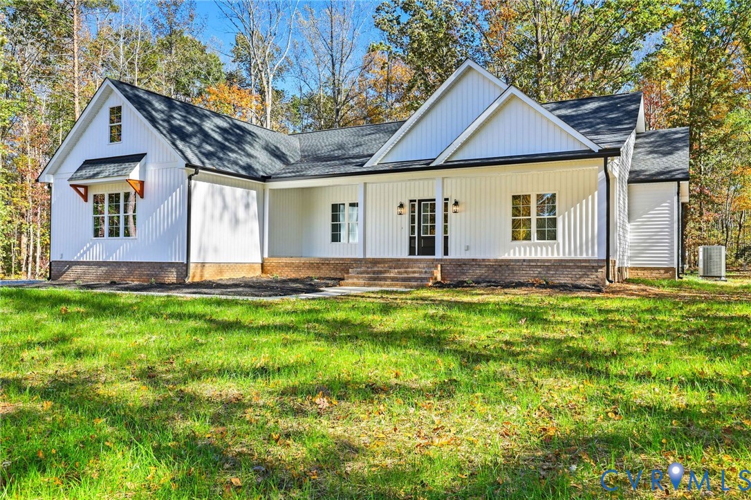 White gabled house with a brick foundation, front steps, and a broad lawn surrounded by autumn trees.