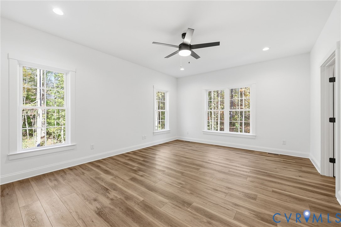 Bright empty room with wood-look flooring, several windows, and a ceiling fan.