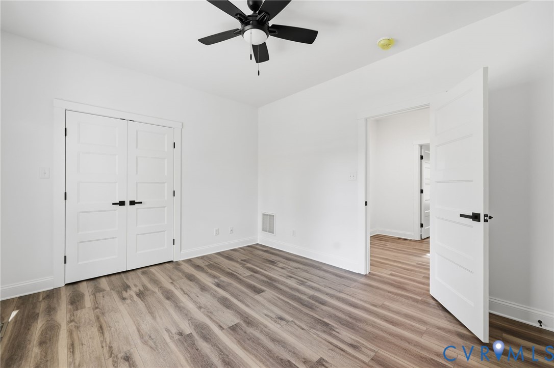 Empty bedroom with double closet doors, wood-look flooring, and a black ceiling fan.