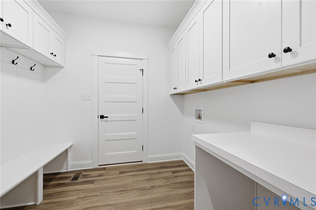 Laundry room with white cabinets, long counters, black hooks, and wood-look flooring.
