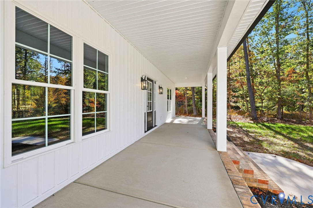 Covered porch with large windows, white siding, and autumn trees beyond.