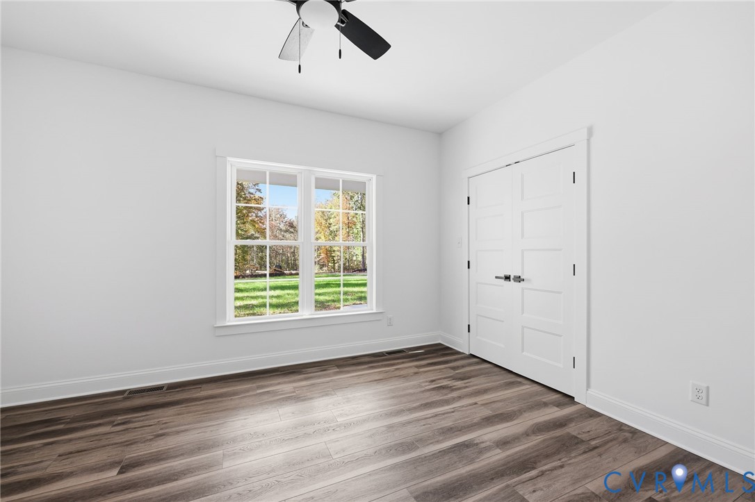 Vacant bedroom with a large lawn-facing window, double closet doors, and gray-brown plank flooring.