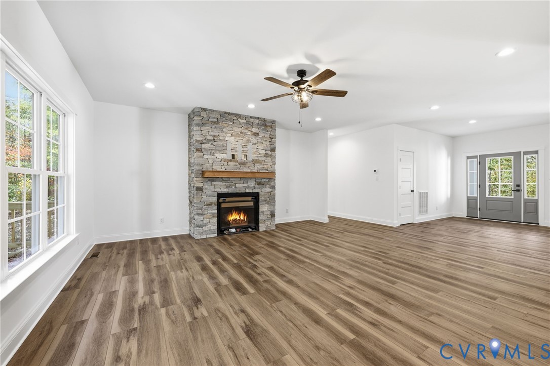 Vacant living room with a stone fireplace, wide-plank flooring, and large windows.