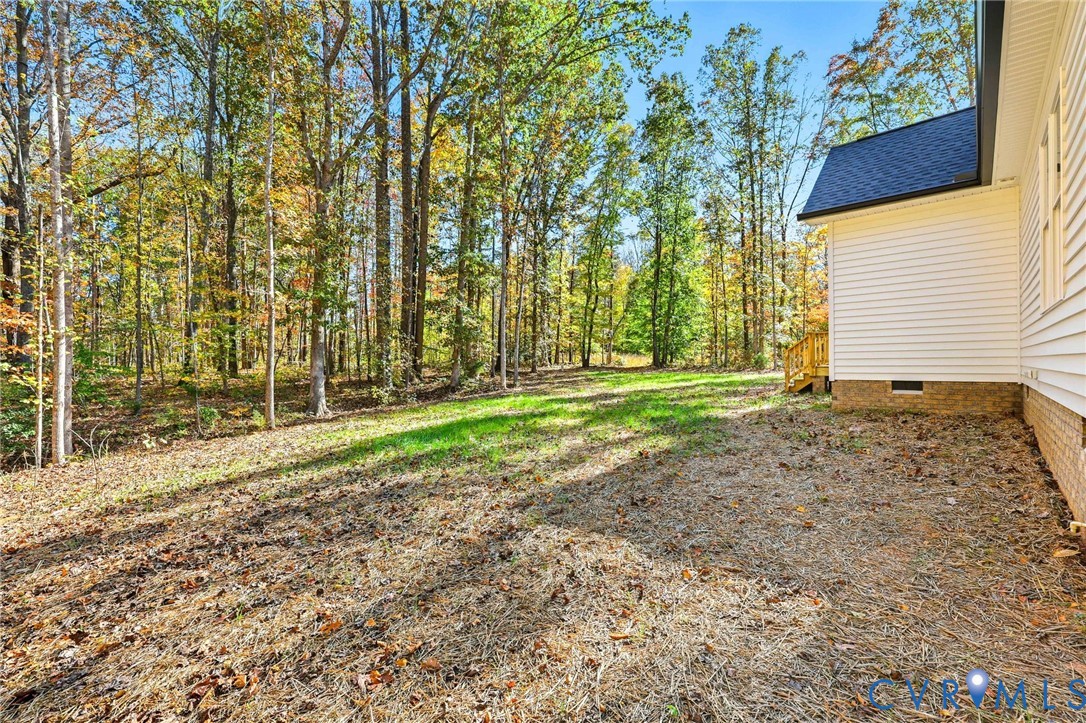 House beside a leaf-covered yard and wooded lot in autumn.