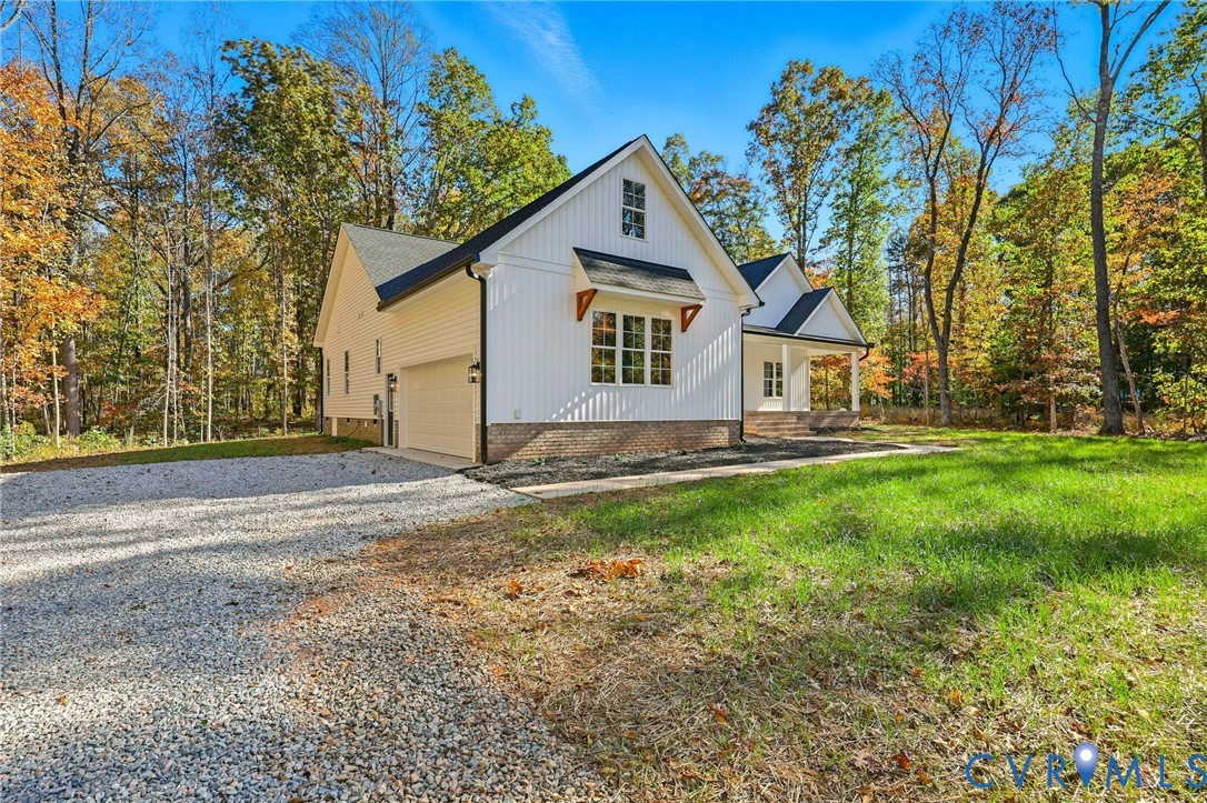 White gabled home with attached garage beside a gravel driveway and wooded autumn yard.
