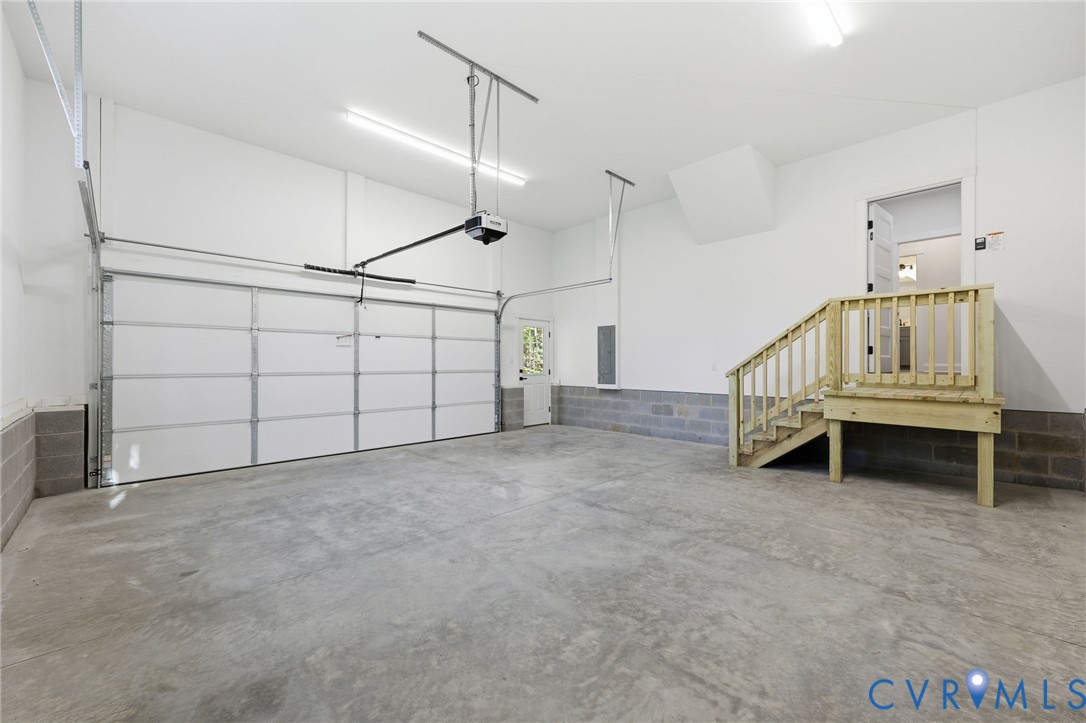 Empty garage with a concrete floor, large garage door, and raised wooden platform with stairs.