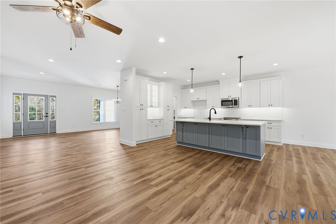Open-plan kitchen with a gray island, white cabinetry, and warm wood floors.