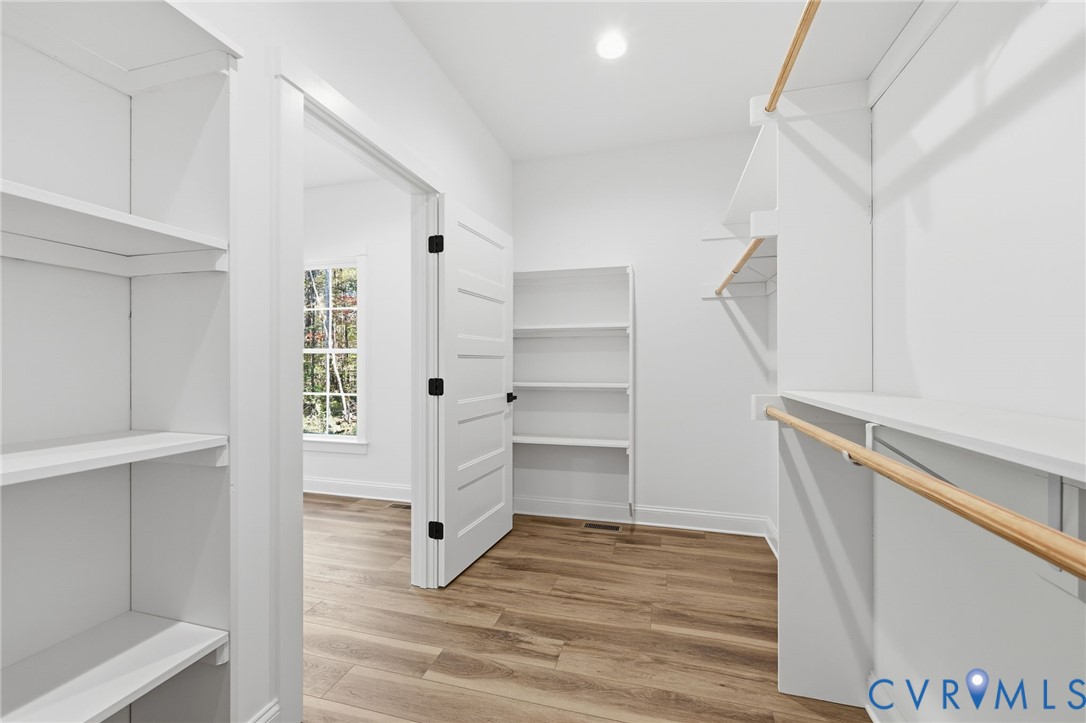 Walk-in closet with built-in shelves, wooden hanging rods, and wood-look flooring.