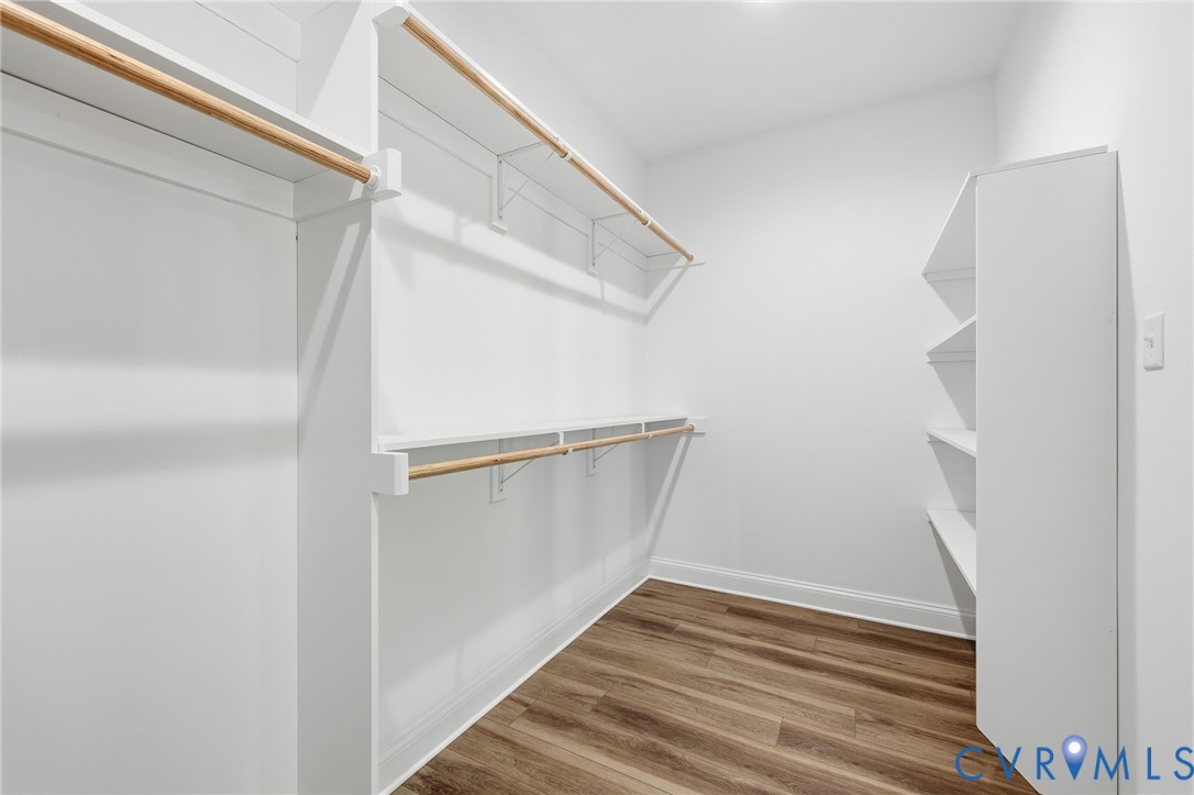 Walk-in closet with built-in shelving, wooden hanging rods, and brown wood-look flooring.