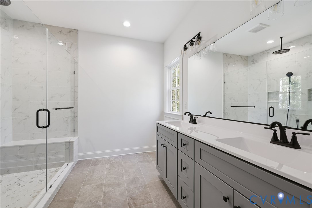 Bright bathroom with a glass-enclosed shower and long gray double vanity.