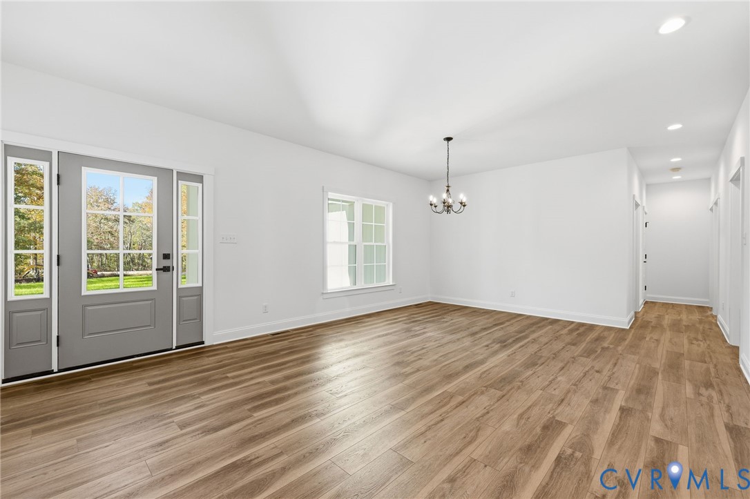 Vacant room with warm wood-look flooring, a gray glass-paneled door, and a chandelier.