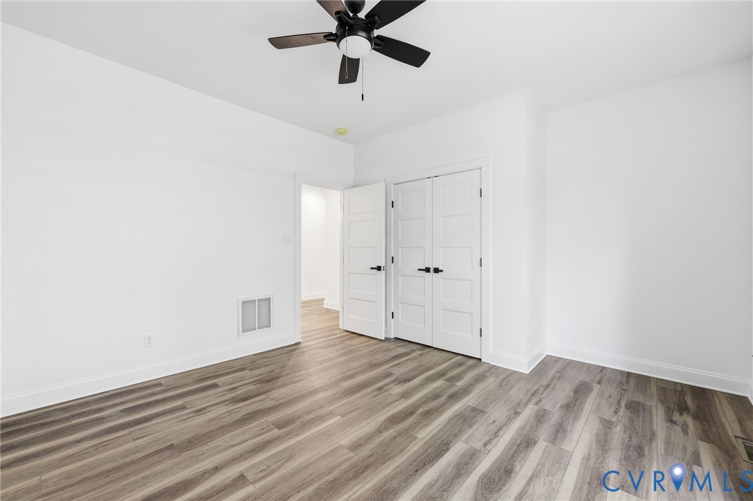 Empty bedroom with plank flooring, a black ceiling fan, and double closet doors.