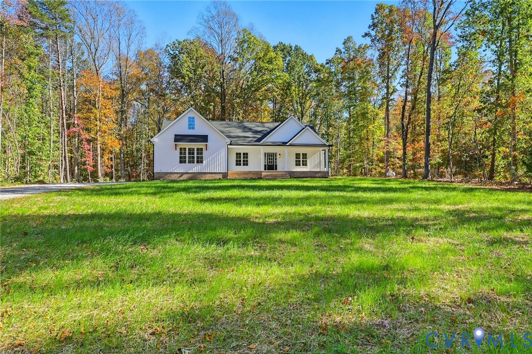 White gabled home set behind a broad lawn, surrounded by autumn trees.