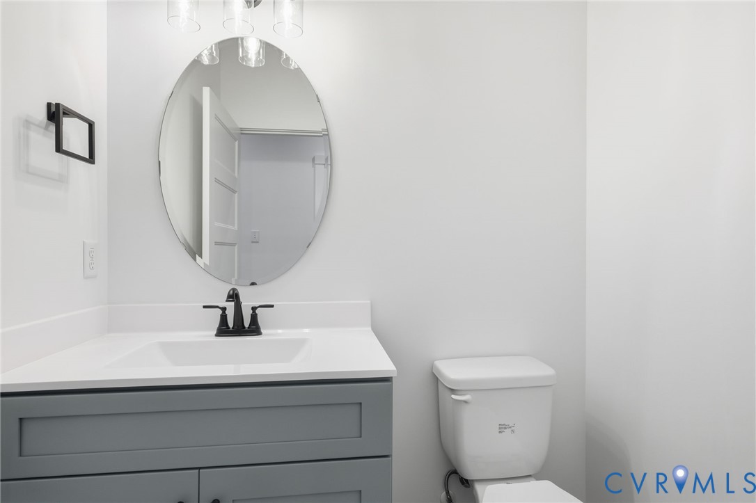 Bathroom with a gray vanity, oval mirror, black faucet, and toilet.