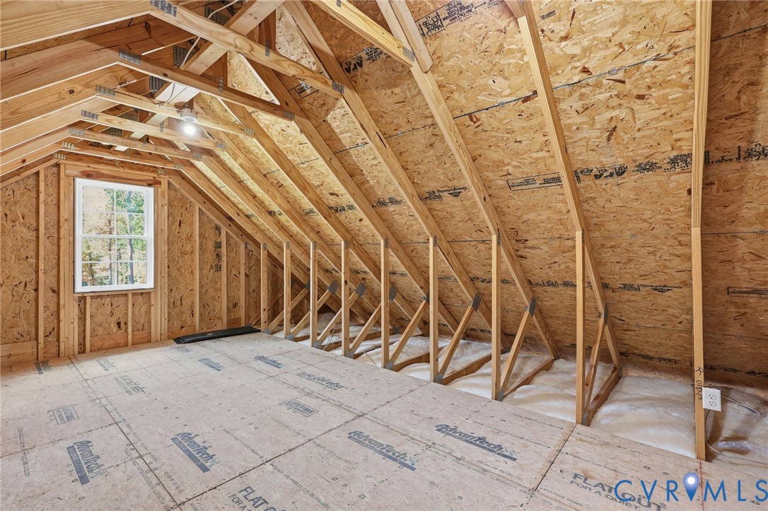 Unfinished attic with exposed wooden trusses, OSB sheathing, and a window.