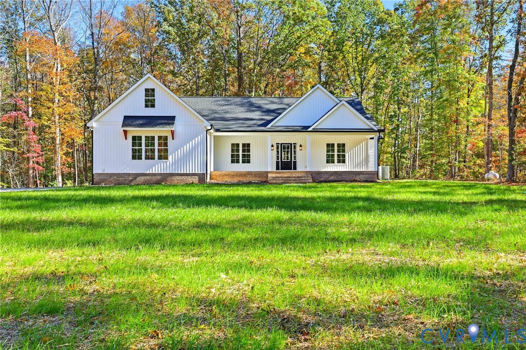 White single-story house with a covered entry, broad green lawn, and autumn trees.