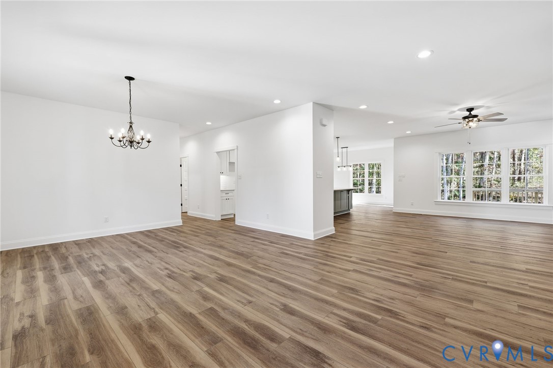 Vacant open-plan living and dining area with wood-look floors, a chandelier, and large windows.