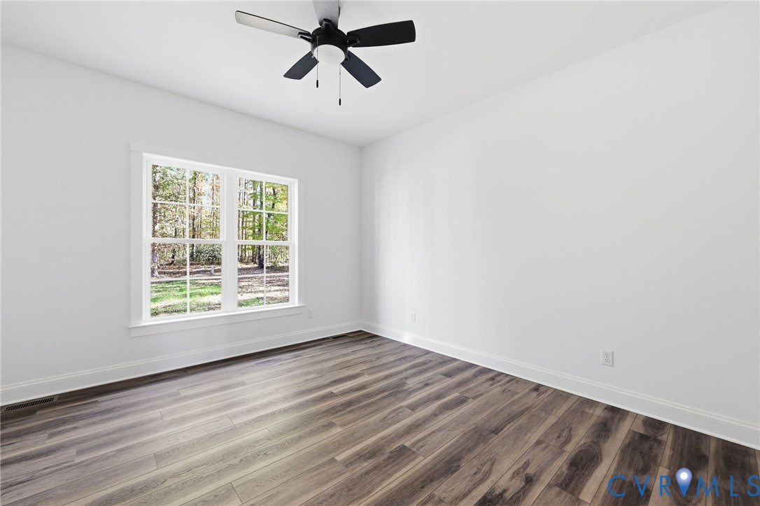 Vacant bedroom with plank flooring, a black ceiling fan, and a large window overlooking trees.