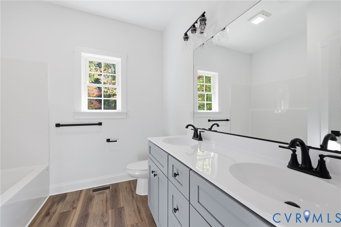 Bright bathroom with a double vanity, large mirror, bathtub, and window overlooking trees.