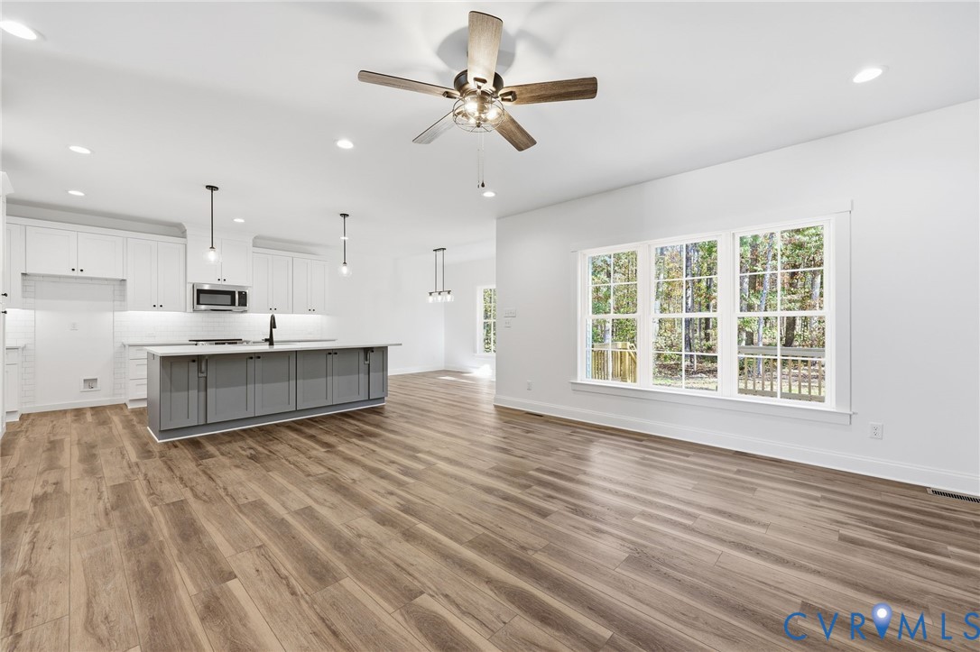 Bright open kitchen with gray island, white cabinetry, wood-look floors, and large windows.