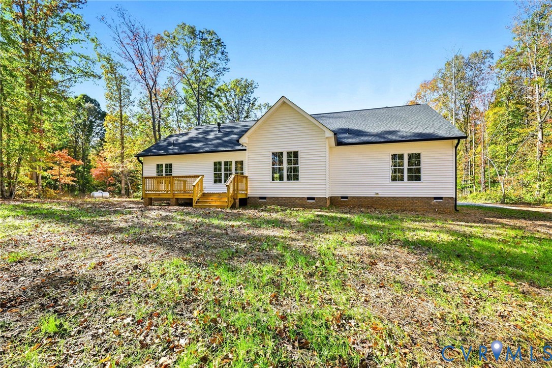 Rear of a light-colored home with a small wooden deck, surrounded by autumn trees.