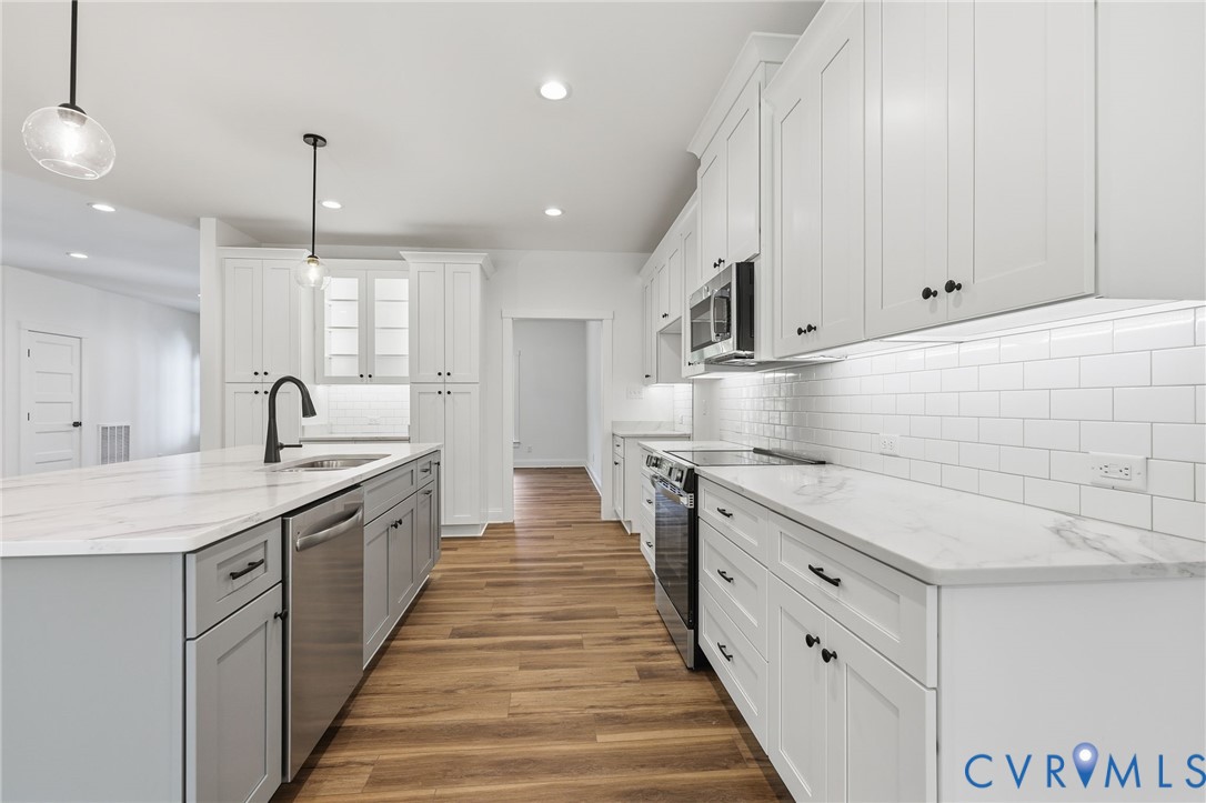 Bright white kitchen with a large island, marble-look counters, stainless steel appliances, and wood floors.