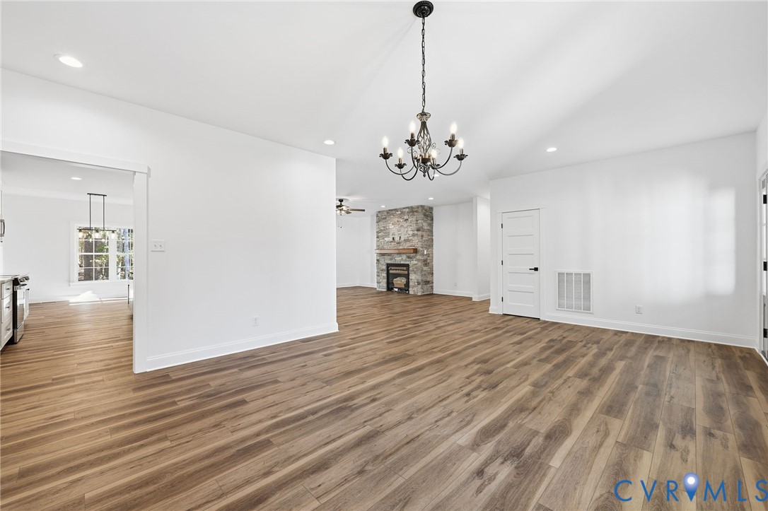 Vacant open-plan living area with wood-look floors, a chandelier, and a stone fireplace.