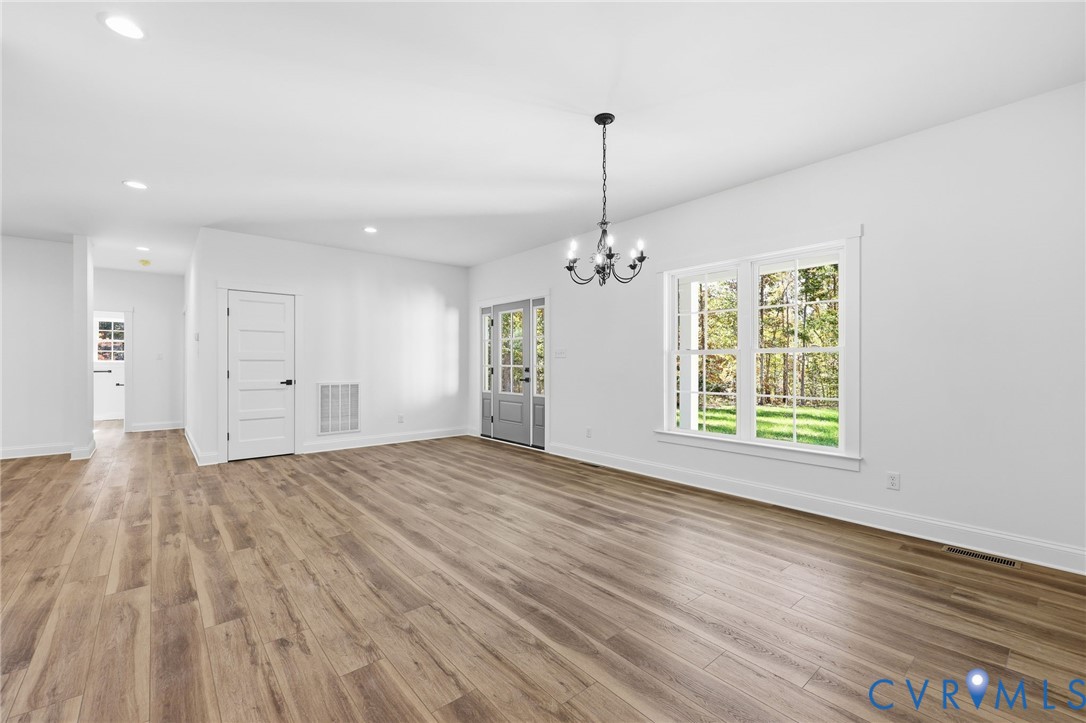 Vacant room with wide-plank wood floors, a black chandelier, French doors, and a large window.