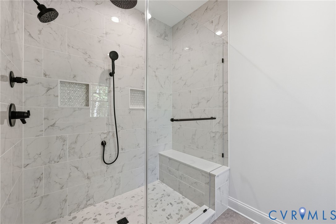 Walk-in shower with marble-look tile, matte black fixtures, glass enclosure, and built-in bench.