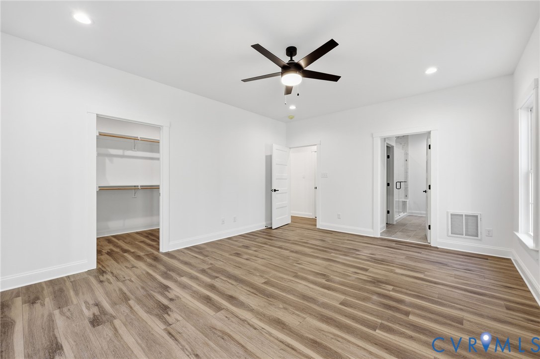 Vacant bedroom with wood-look flooring, ceiling fan, open closet, and adjoining bathroom.
