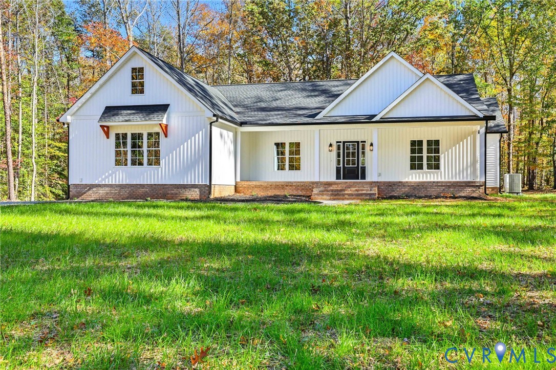 White gabled home with a brick foundation, broad lawn, and autumn trees behind it.