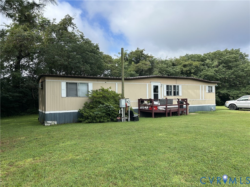 Beige manufactured home with a raised red deck, broad lawn, and mature trees.