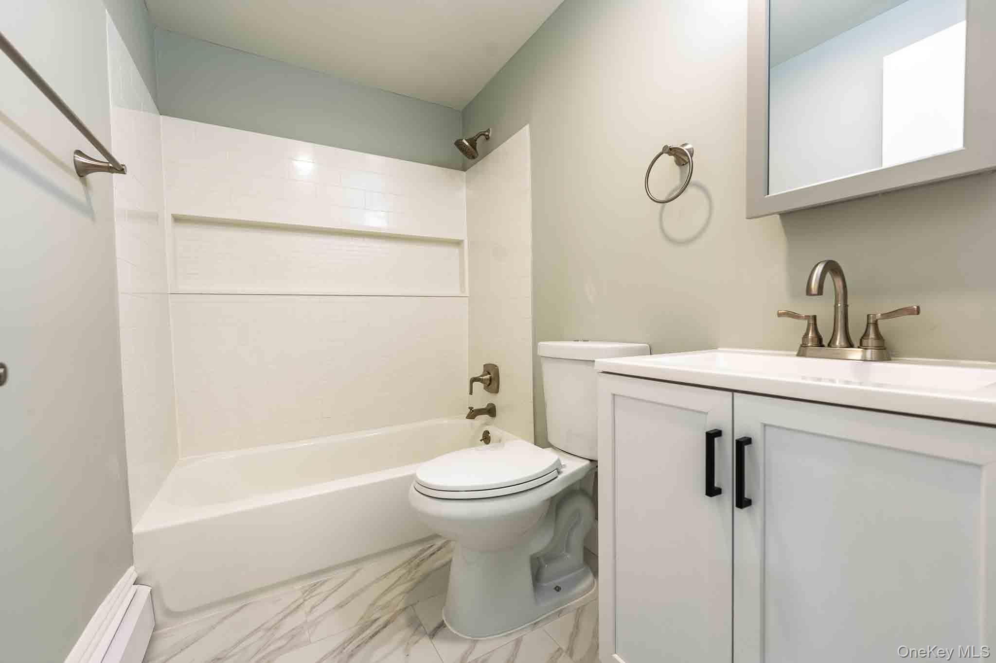 Bathroom with a white tub, toilet, and vanity with marble-patterned tile flooring.