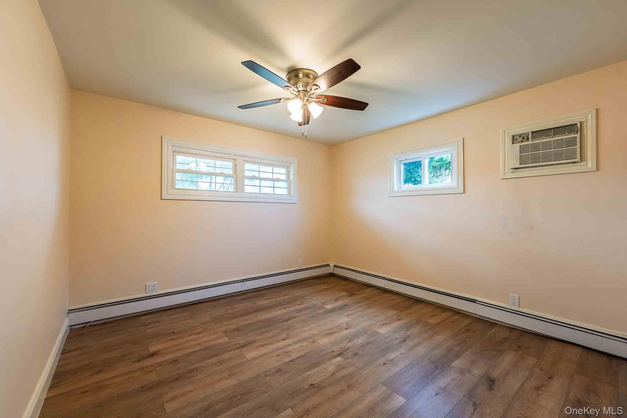 Vacant room with wood-look flooring, a ceiling fan, baseboard heating, and a window air conditioner.