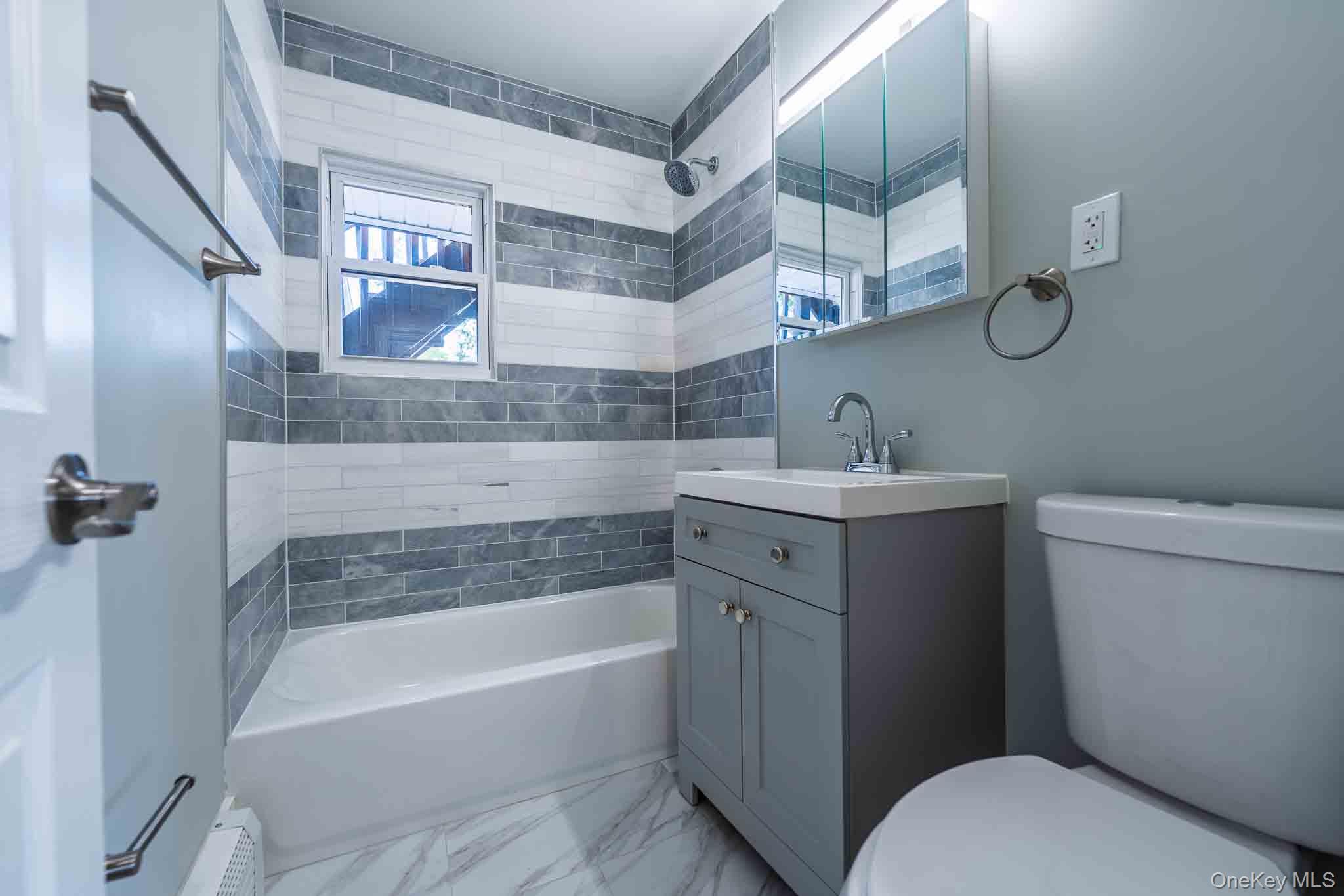 Bathroom with a gray vanity, white tub, and gray-and-white tiled shower surround.