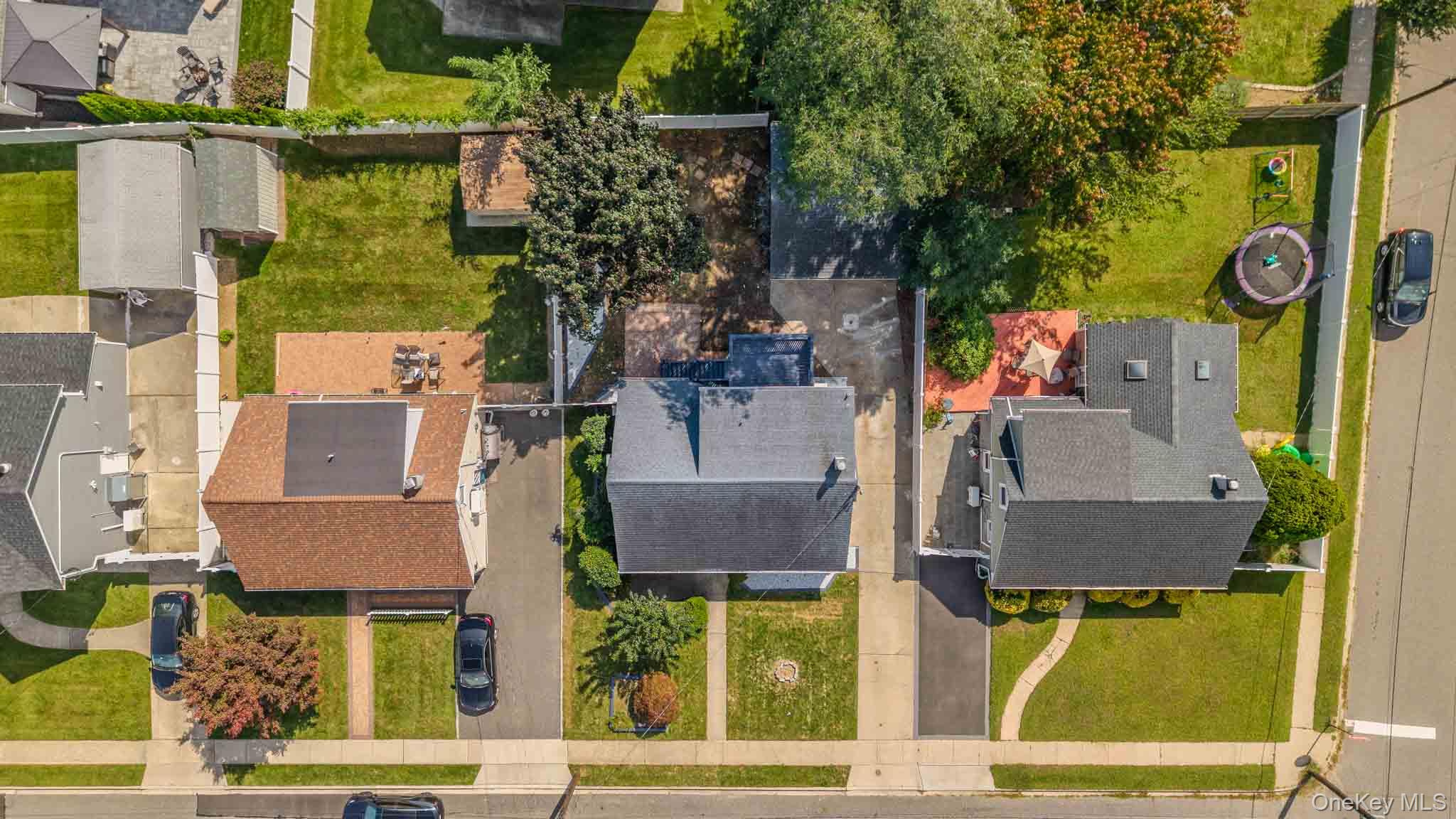 Aerial view of a gray-roofed home with a paved backyard, surrounded by neighboring houses and lawns.