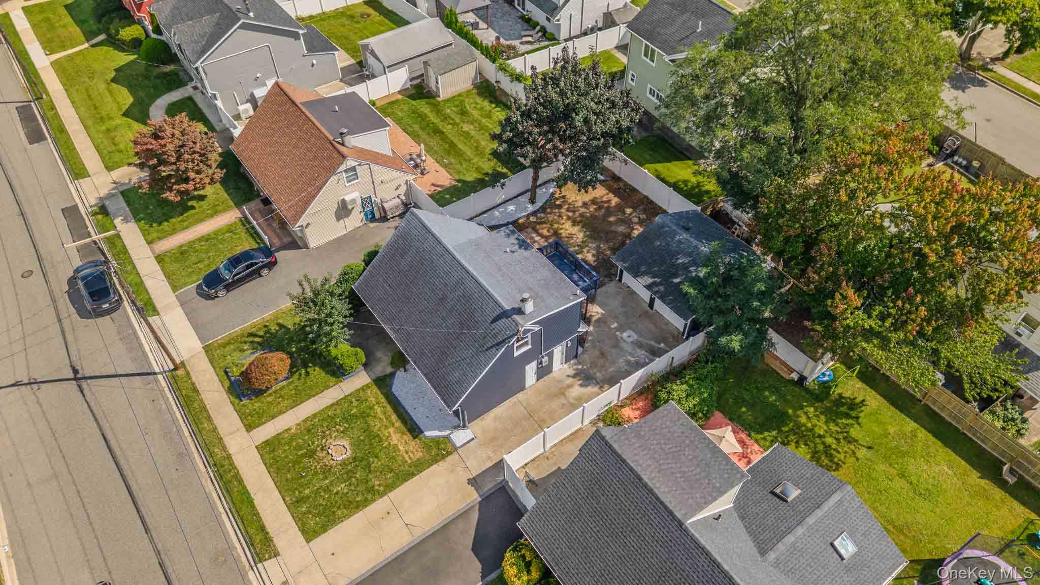 Aerial view of a dark blue-gray house with a fenced yard and paved driveway.