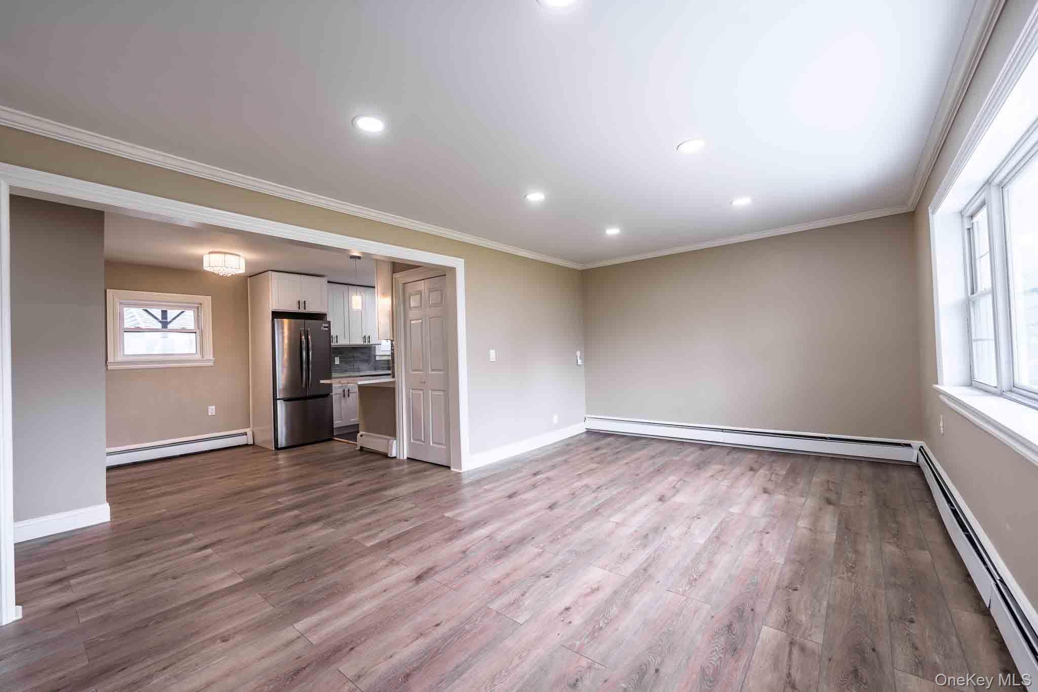 Unfurnished living room with wood-look floors, large windows, and an open kitchen.