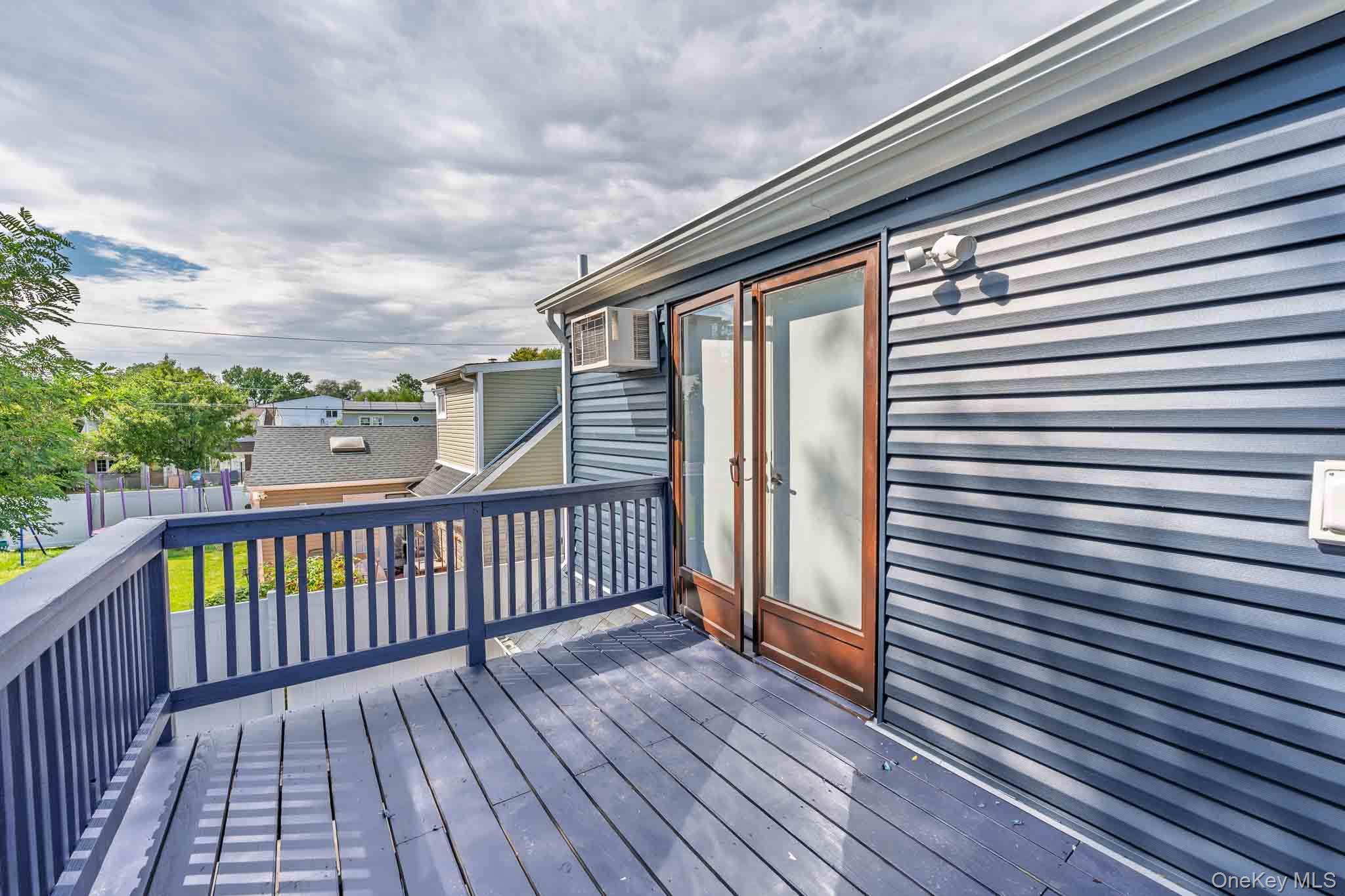 Raised gray deck with blue railings beside a blue-gray house, viewed toward wood-framed glass doors.