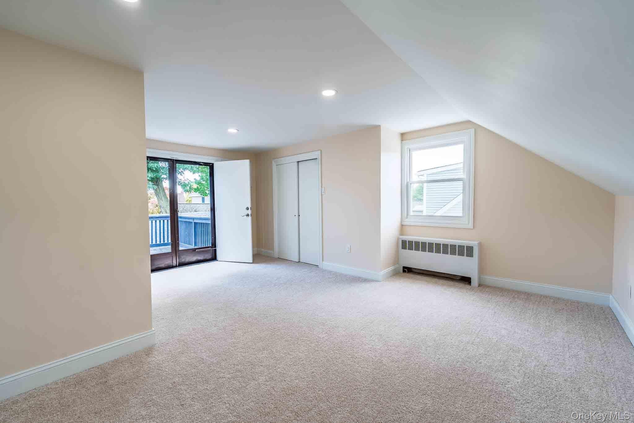 Empty carpeted upstairs room with a sloped ceiling and sliding doors to a balcony.