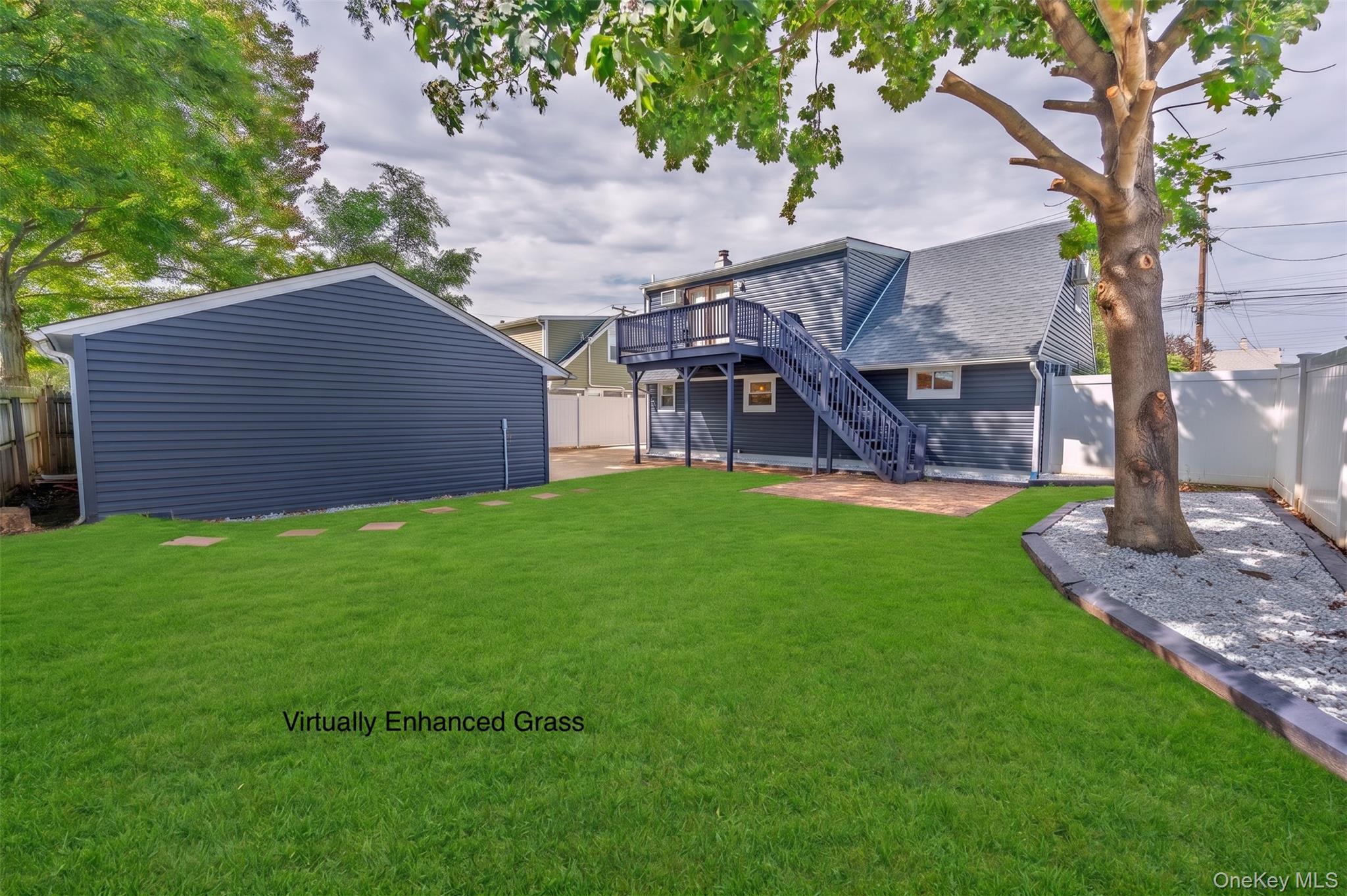 Backyard with a dark blue house, elevated deck, detached garage, and broad green lawn.