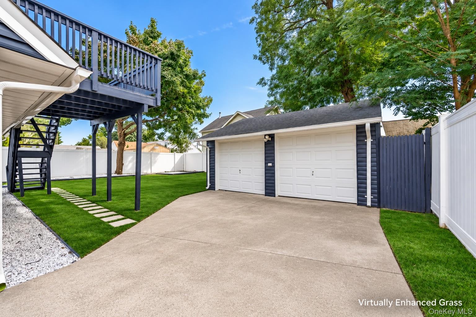 Two-door garage and wide driveway beside a fenced lawn and raised deck.