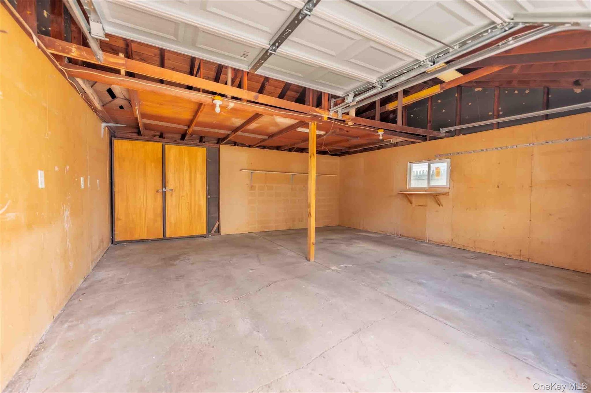 Empty garage with exposed roof framing, a concrete floor, and wooden storage doors.