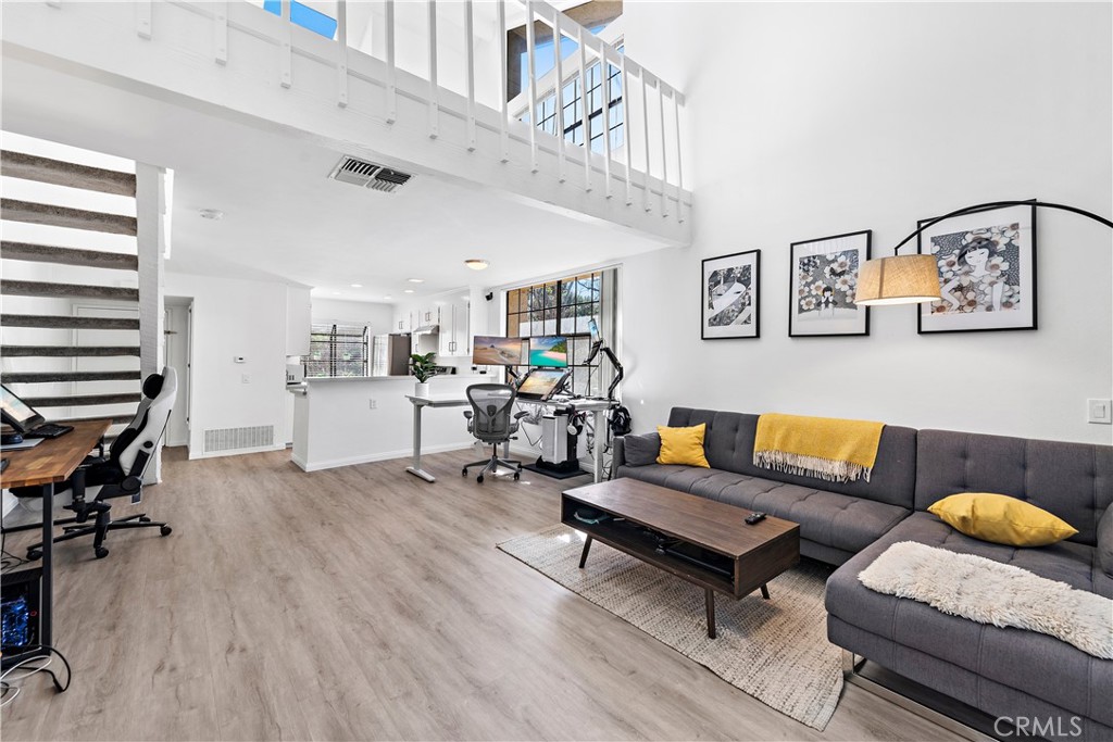 Loft-style living room with a gray sectional, open mezzanine, and a home office workstation.