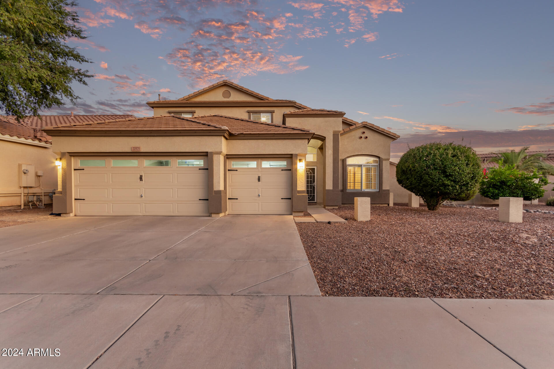 Two-story stucco home with a tile roof, two-car garage, and desert landscaping at dusk.