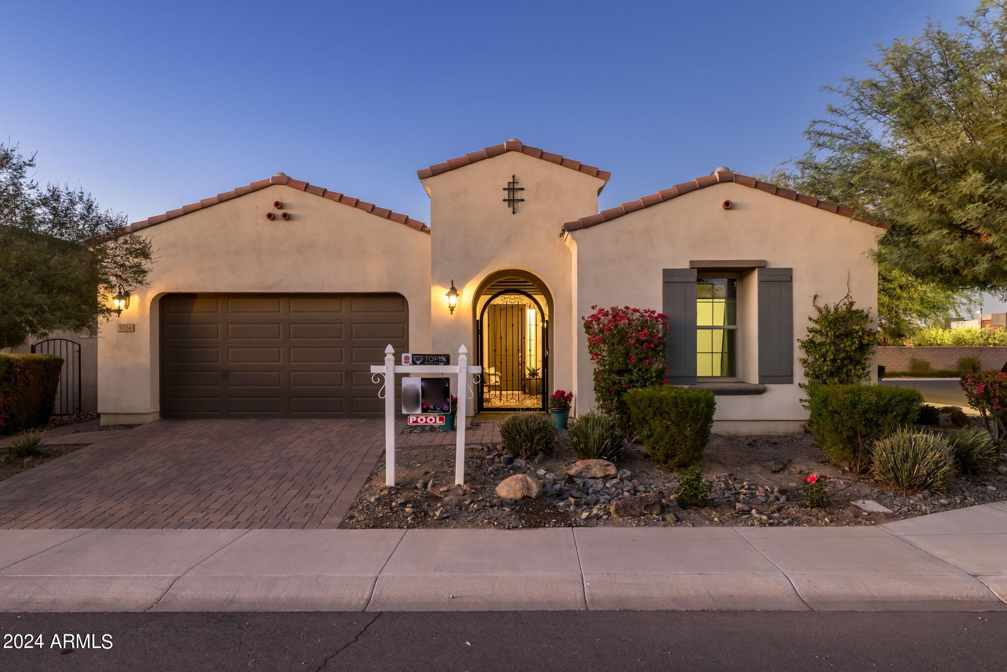 Stucco home with a tiled roof, arched entry gate, dark garage, and landscaped front yard.