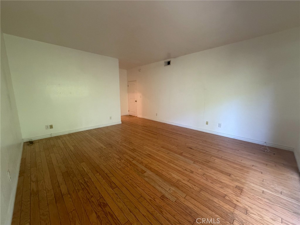 Vacant room with hardwood floors, white walls, and a closet door.
