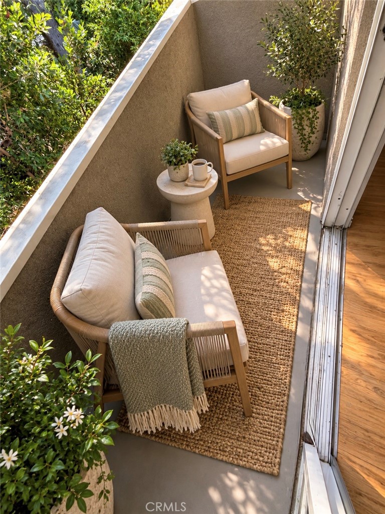 Furnished balcony with wicker seating, potted plants, and a woven rug beside an open sliding door.